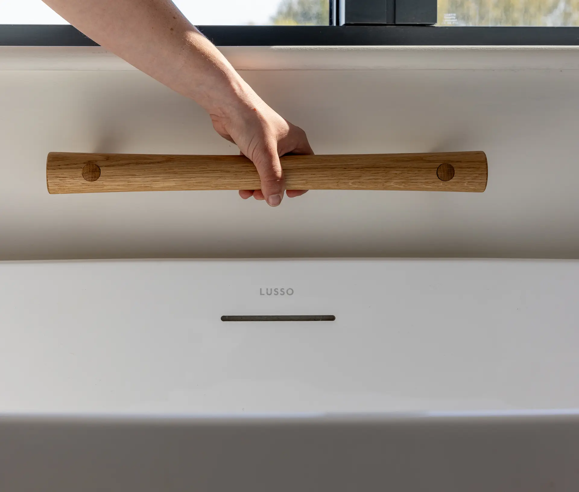 Hand gripping an oak grab rail above a white bathtub.
