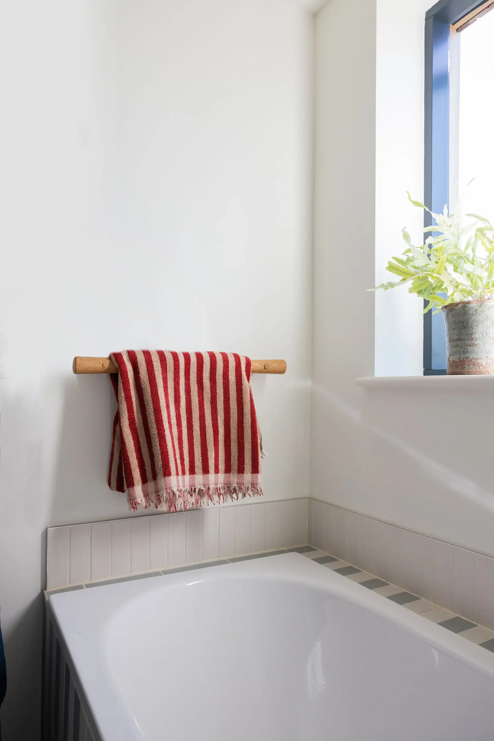 Striped towel hanging over an oak grab rail above a bathtub.