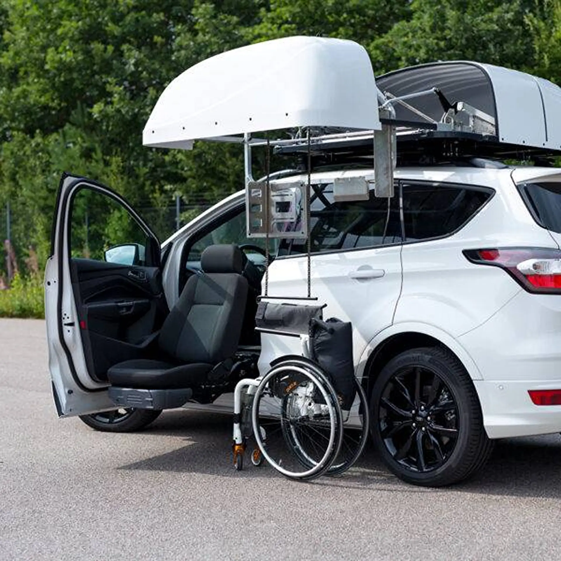 Close-up of topper's open lid lowering a folded wheelchair beside a car door.