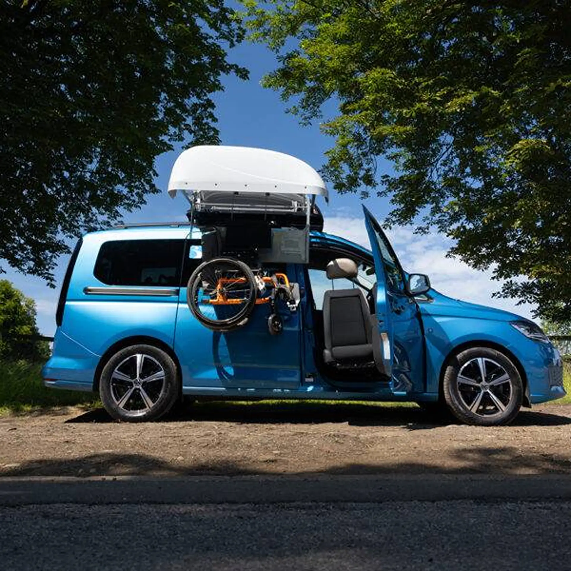 Blue people-carrier with topper open, wheelchair held above the passenger door.
