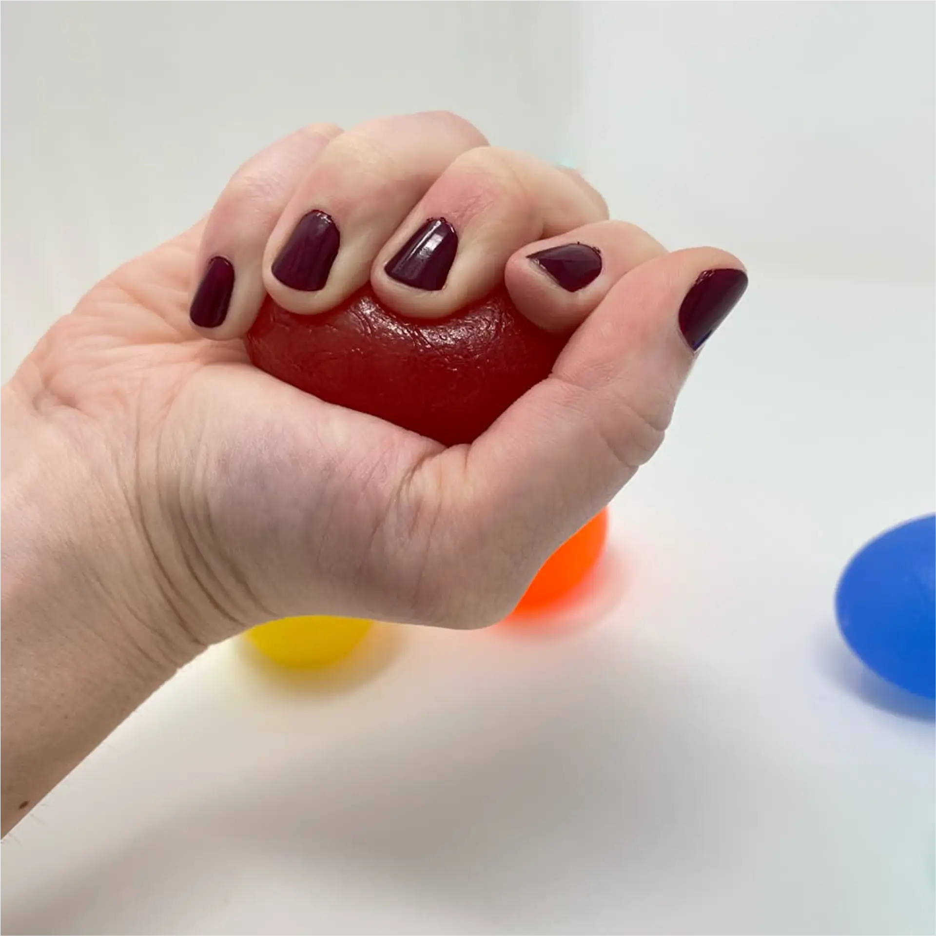 Hand squeezing red egg-shaped hand exerciser with other colors blurred behind.