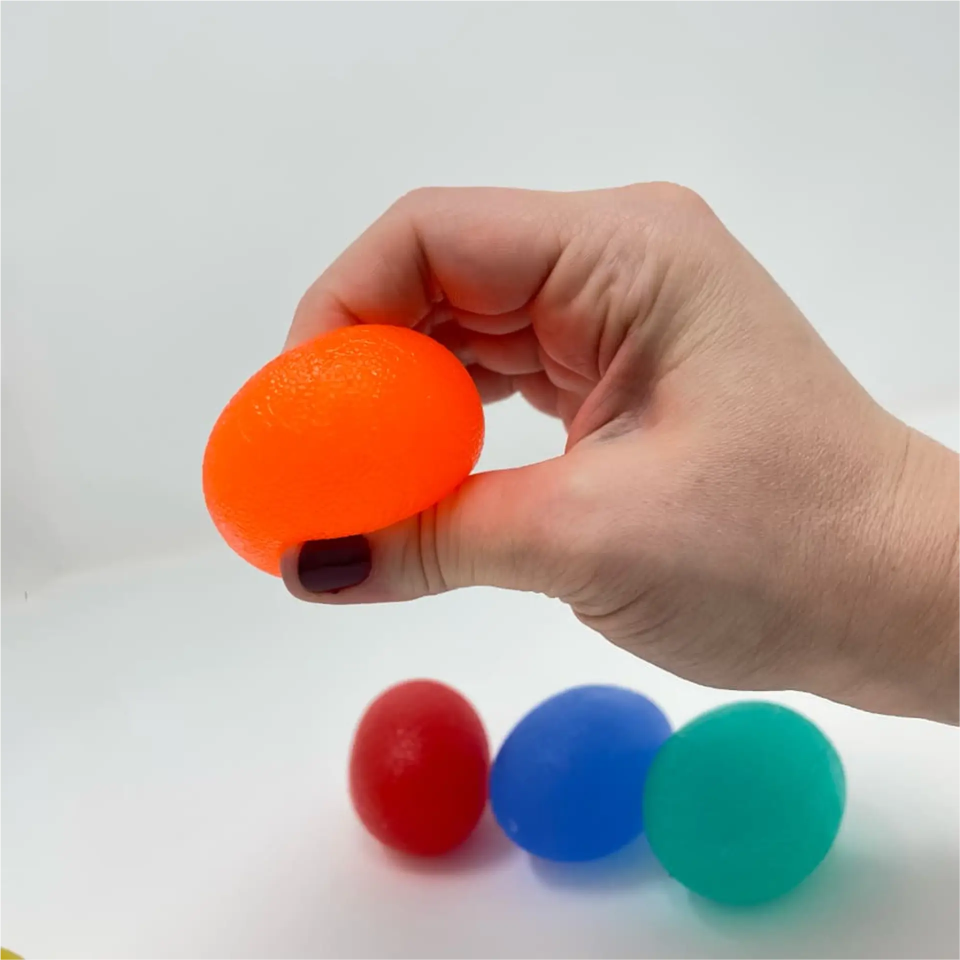 Hand pinching orange egg-shaped exerciser with red, blue, and teal ones nearby.