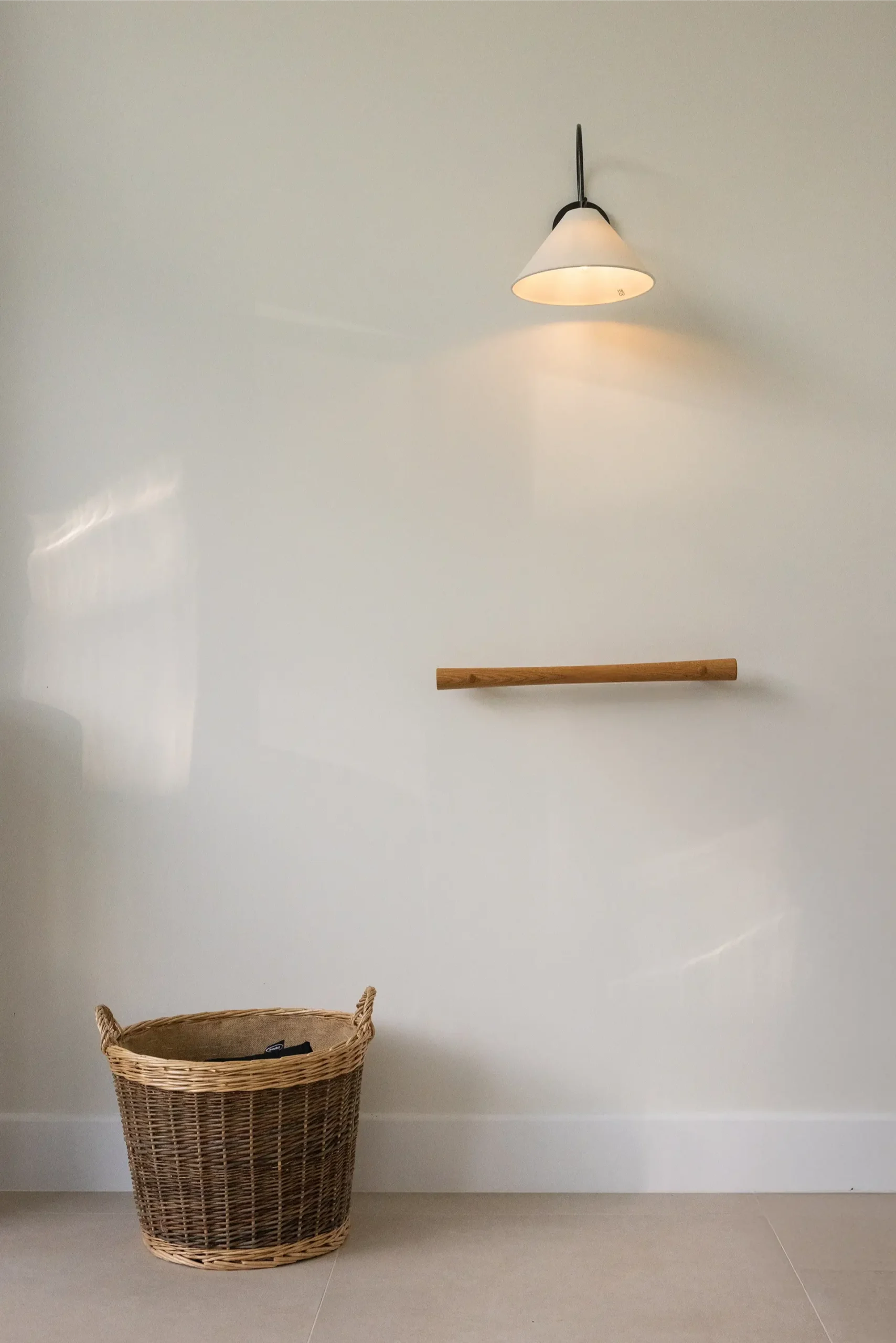 Oak grab rail mounted on wall beside a wicker basket and lit wall lamp.