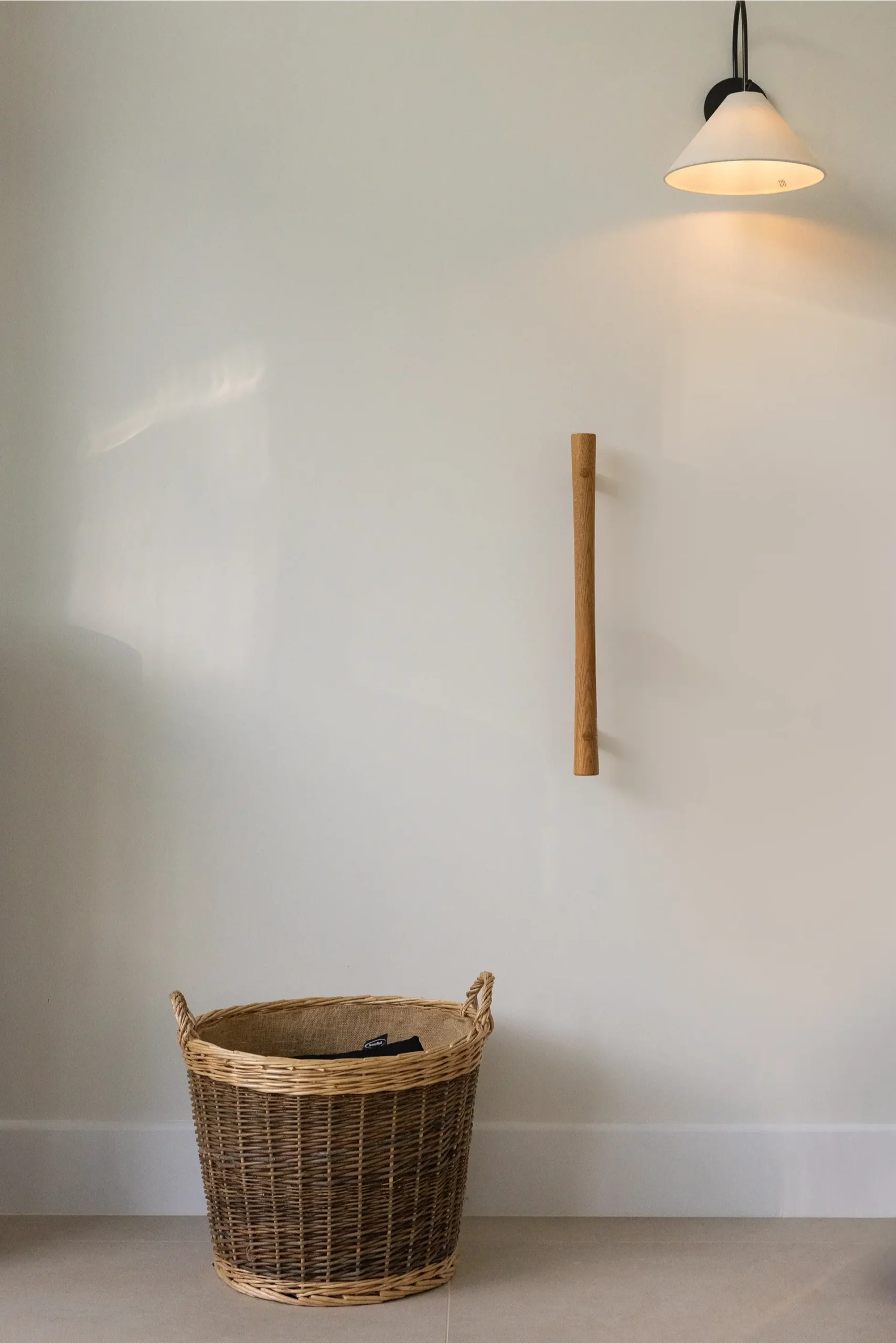 Vertical oak grab rail mounted on wall beside a wicker basket and lamp.