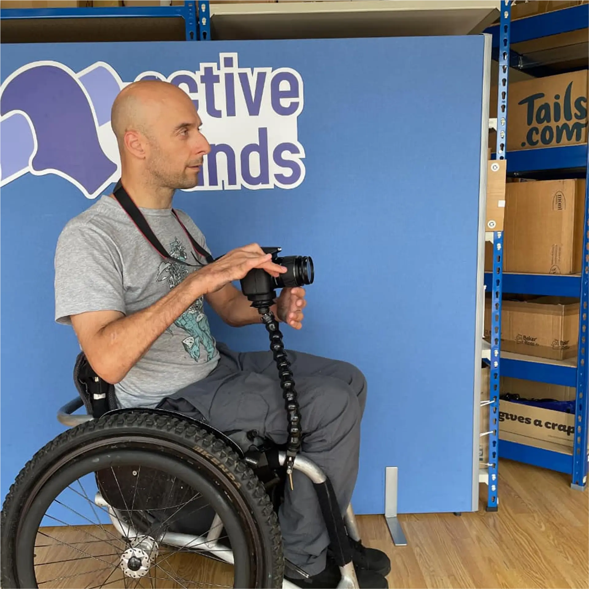 Man in wheelchair holding camera on flexible arm mount at Active Hands office.