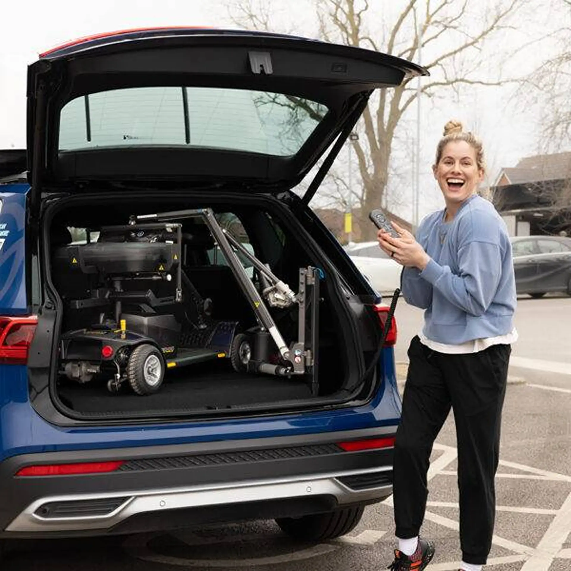 Woman holding the remote as a scooter loads into her car's boot.