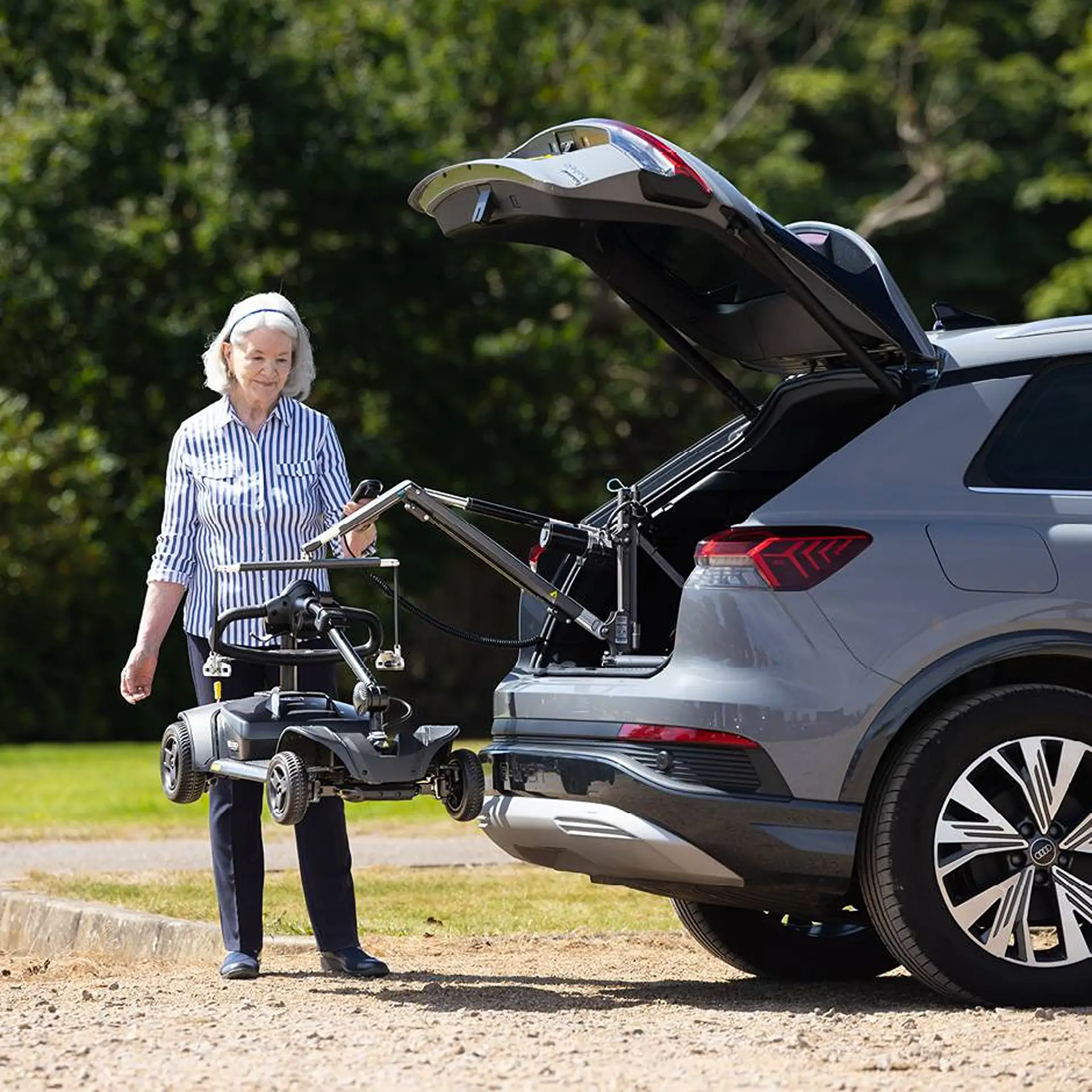 Elderly woman using the remote to lower a scooter from an Audi's boot.