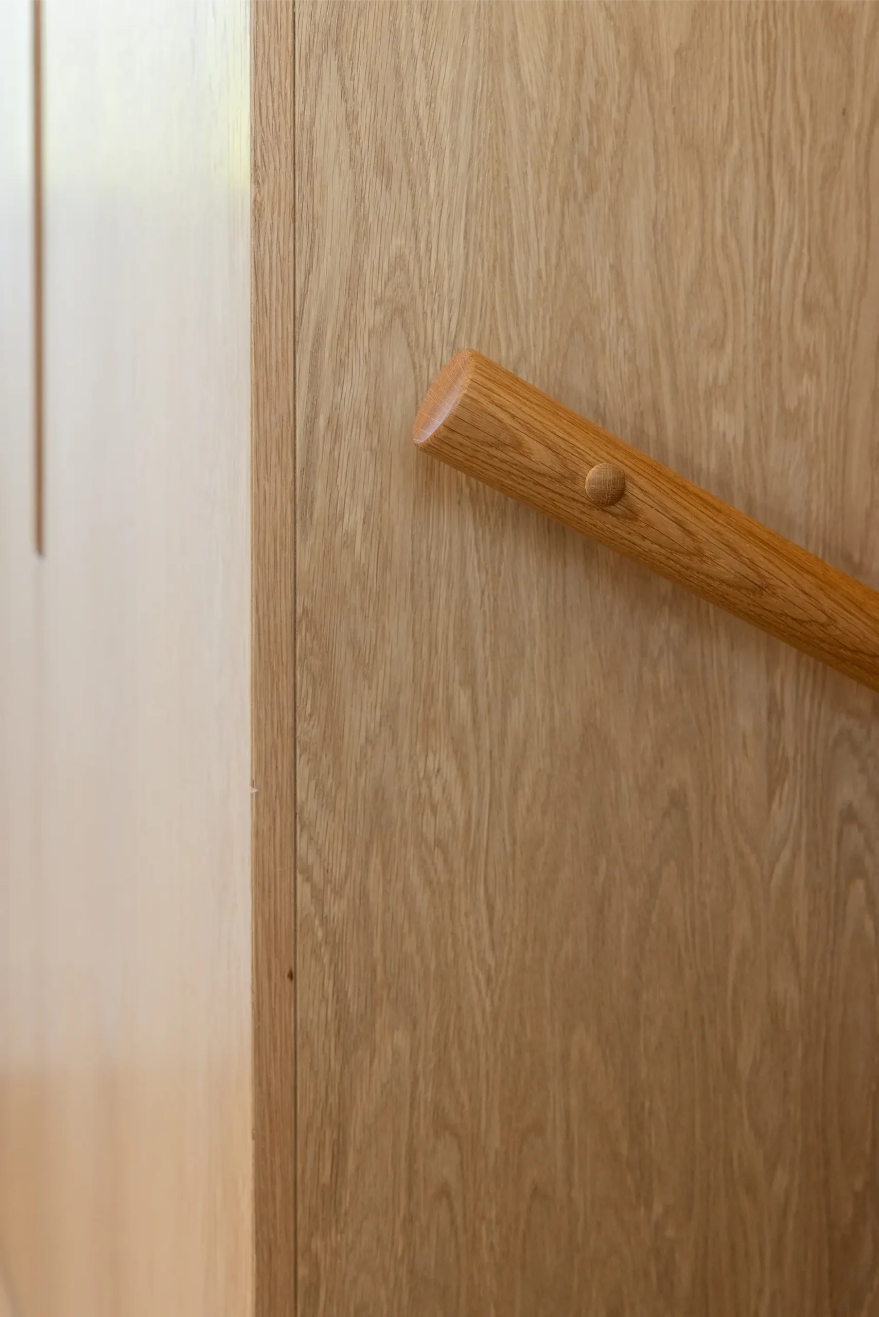 Close-up of an oak grab rail mounted on a wood-paneled wall.