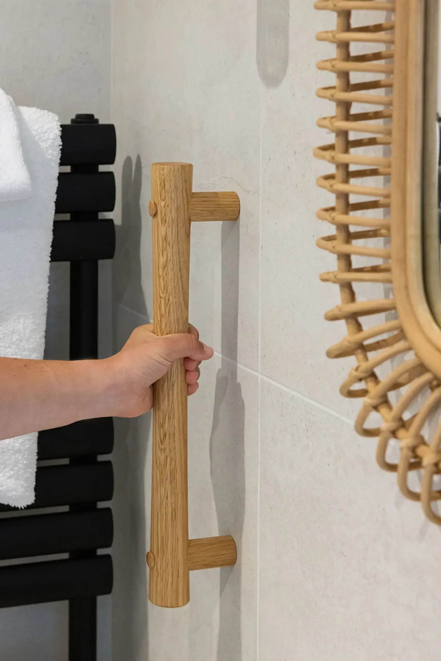 Hand gripping an oak grab rail in a tiled bathroom.