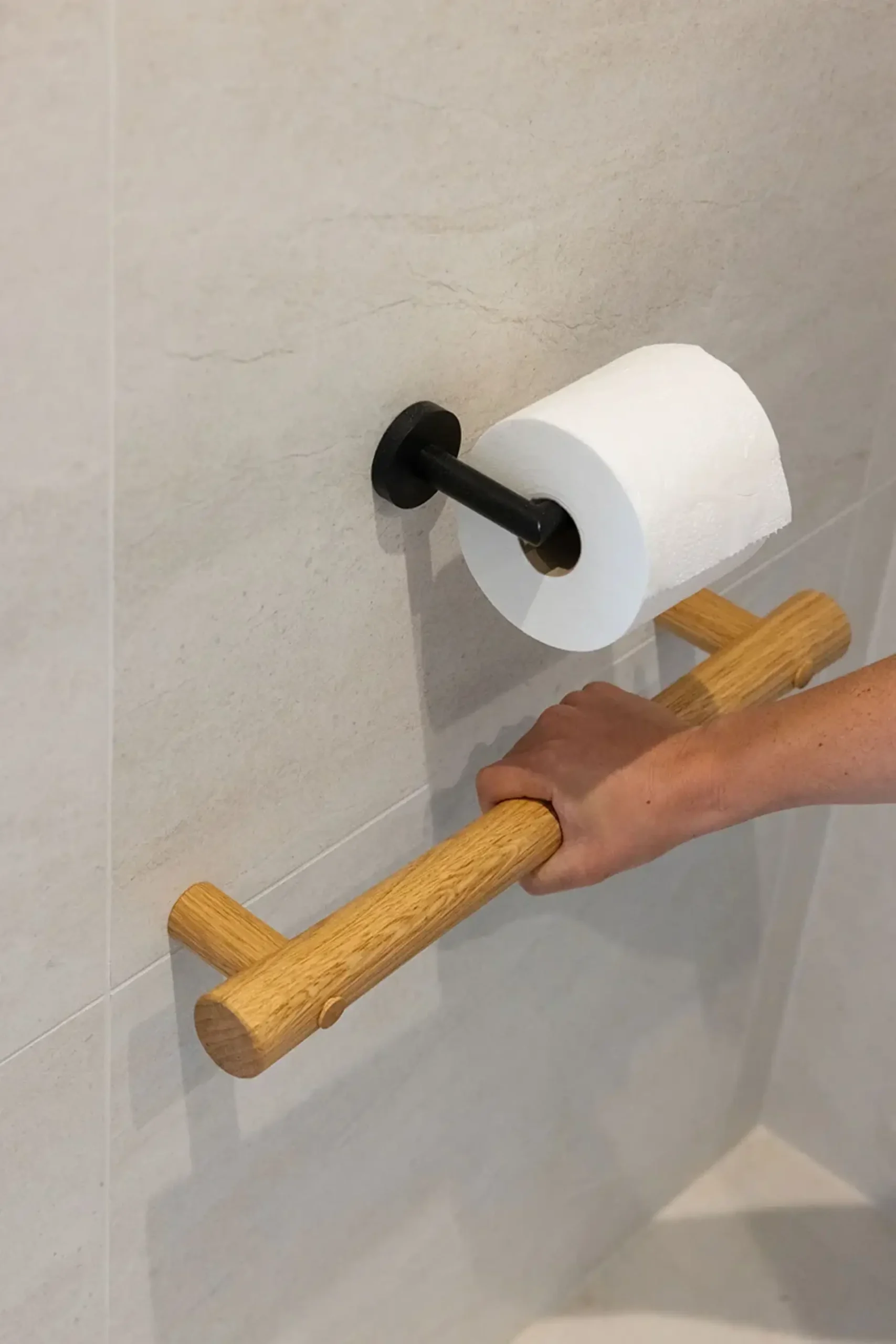 Hand gripping an oak grab rail below a toilet roll holder.