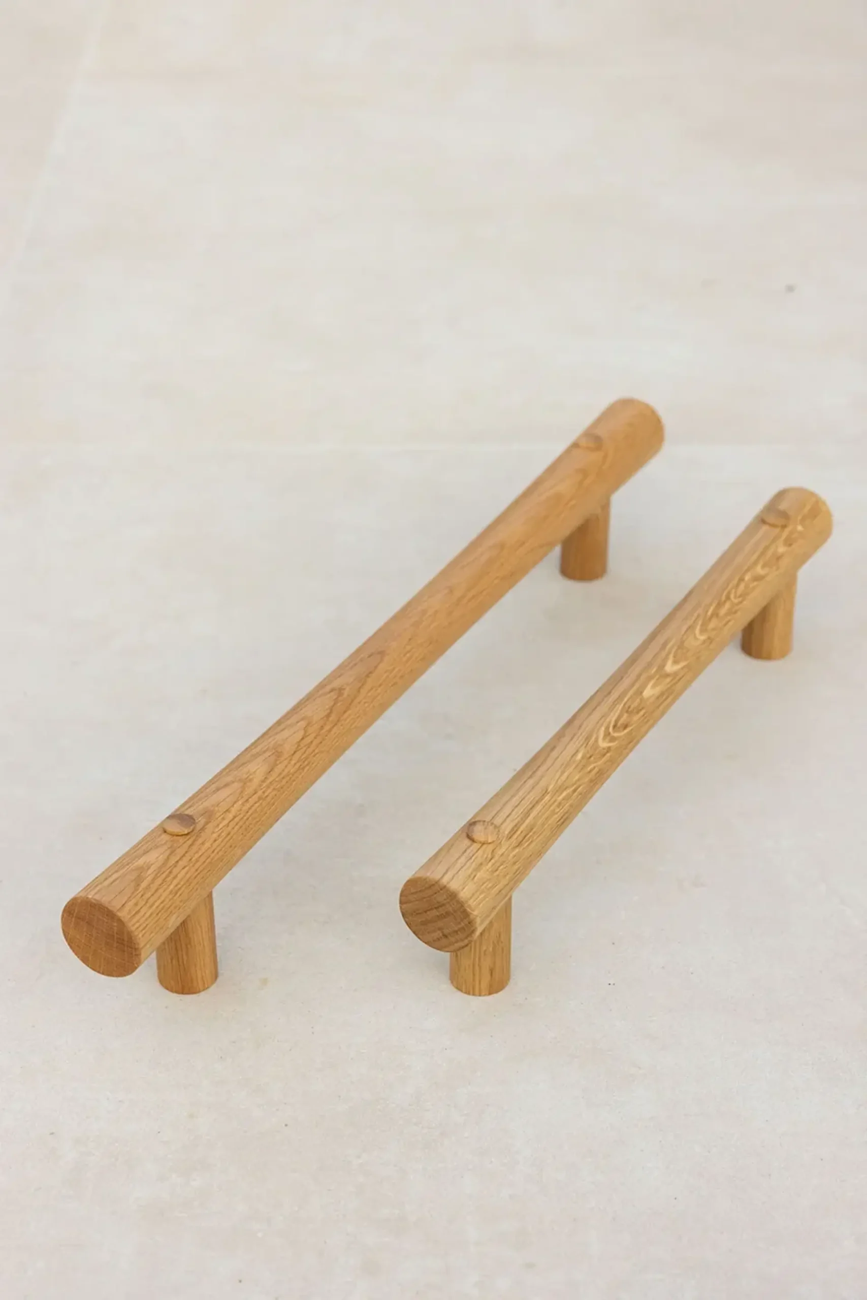 Two oak grab rails with T-ends standing upright on a light surface.