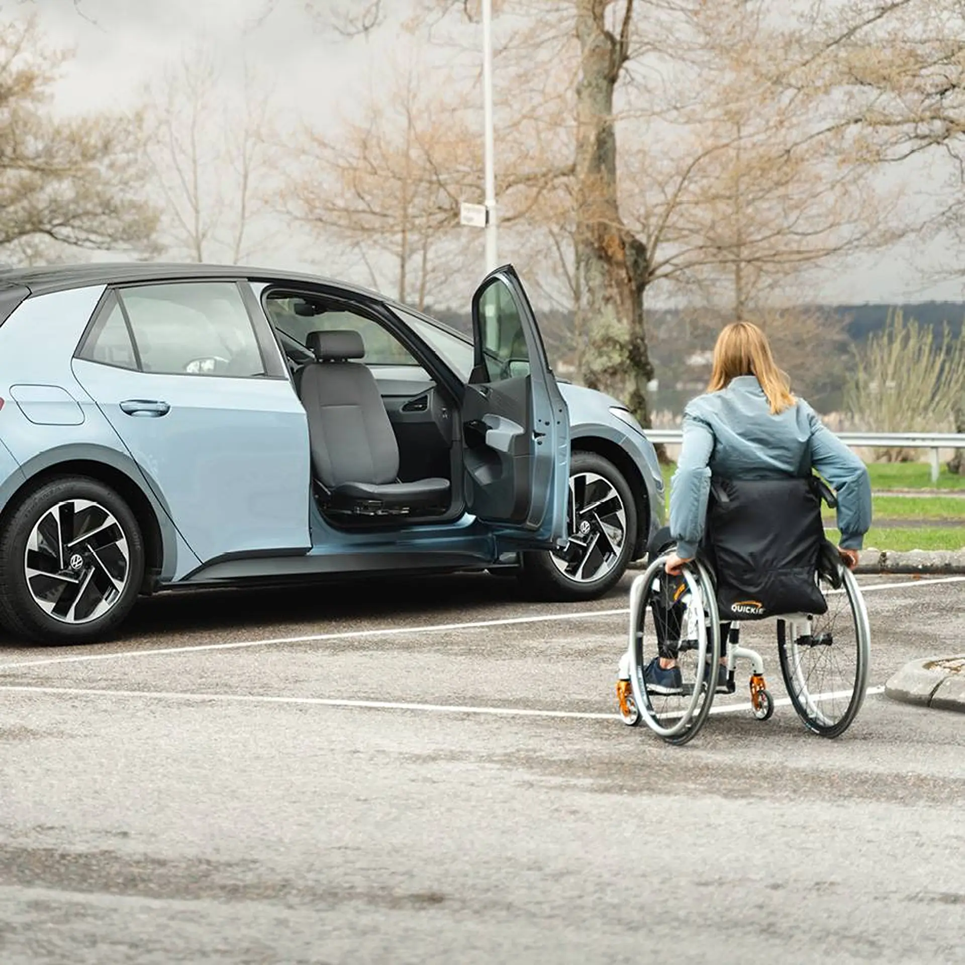 Wheelchair user approaching a car with its front seat swivelled out through the open door.