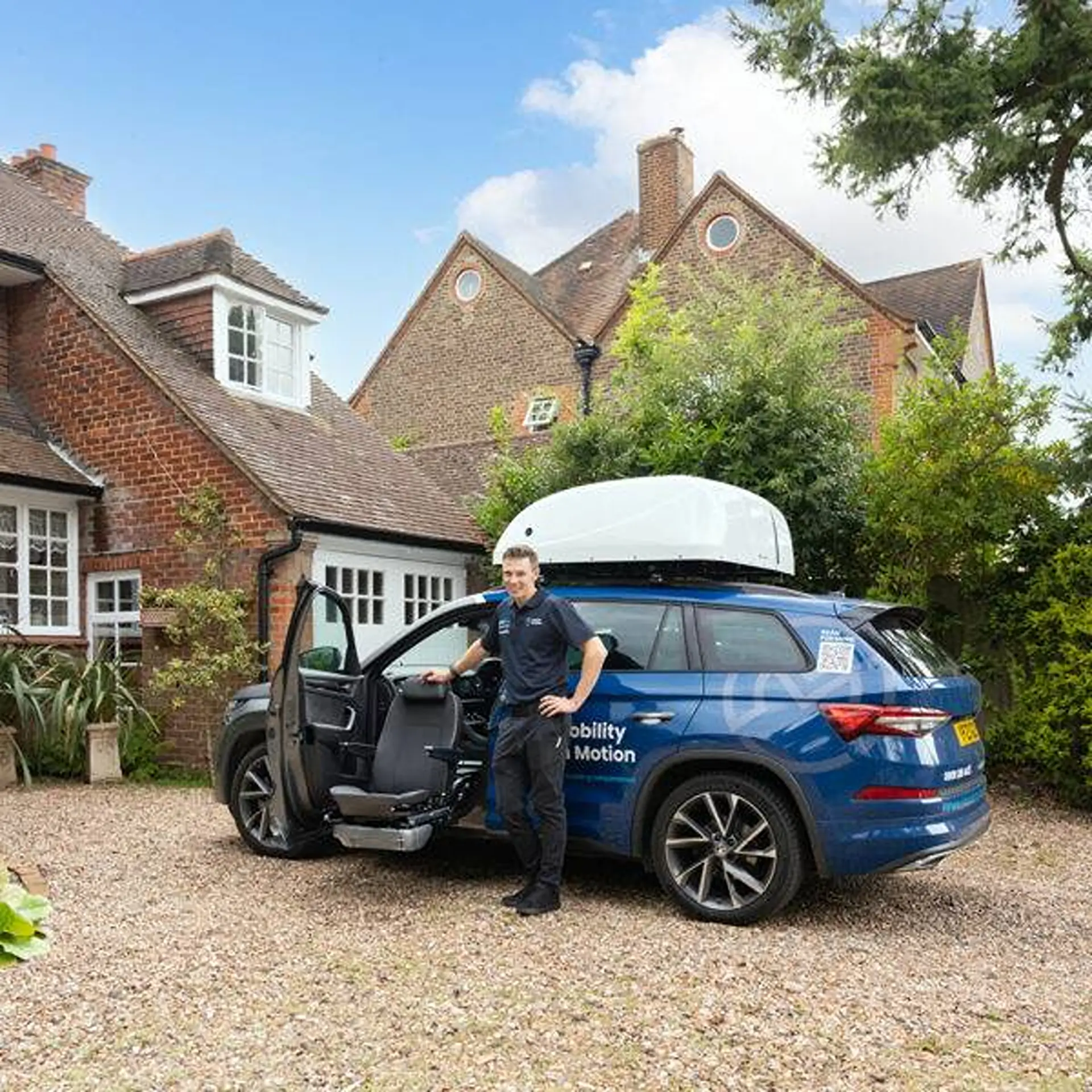 Man standing beside his SUV with the front seat swivelled out, roof box fitted, driveway setting.