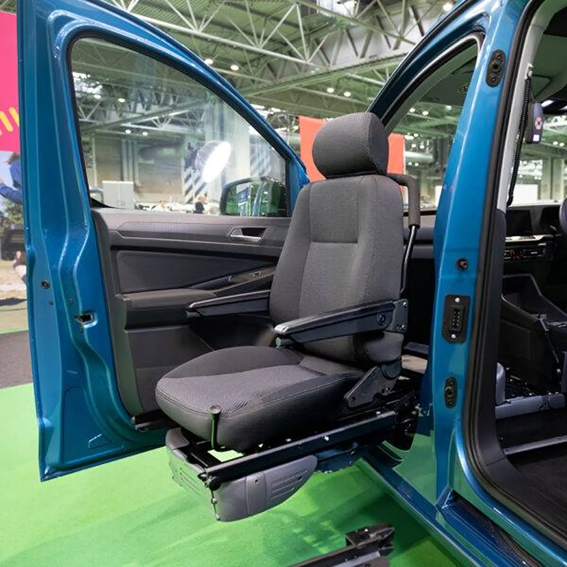 Empty swivelled seat extended through a car's open door at a trade show.