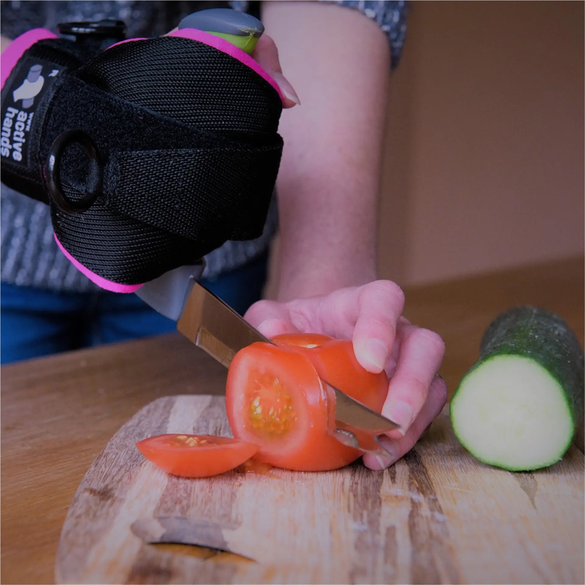 Wrist-mounted knife slicing cherry tomato on board.