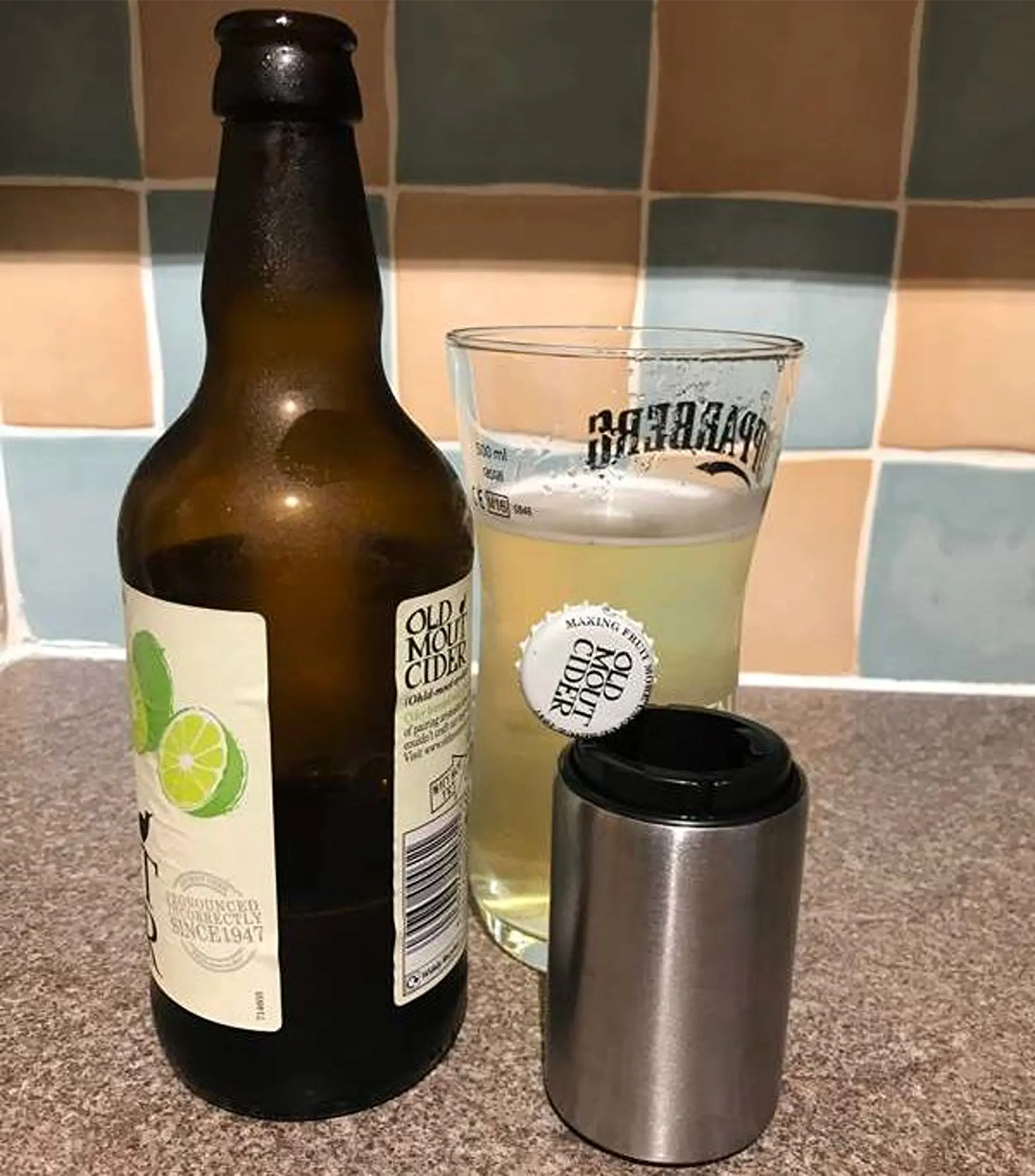 Cider bottle, filled glass, and metal bottle opener.