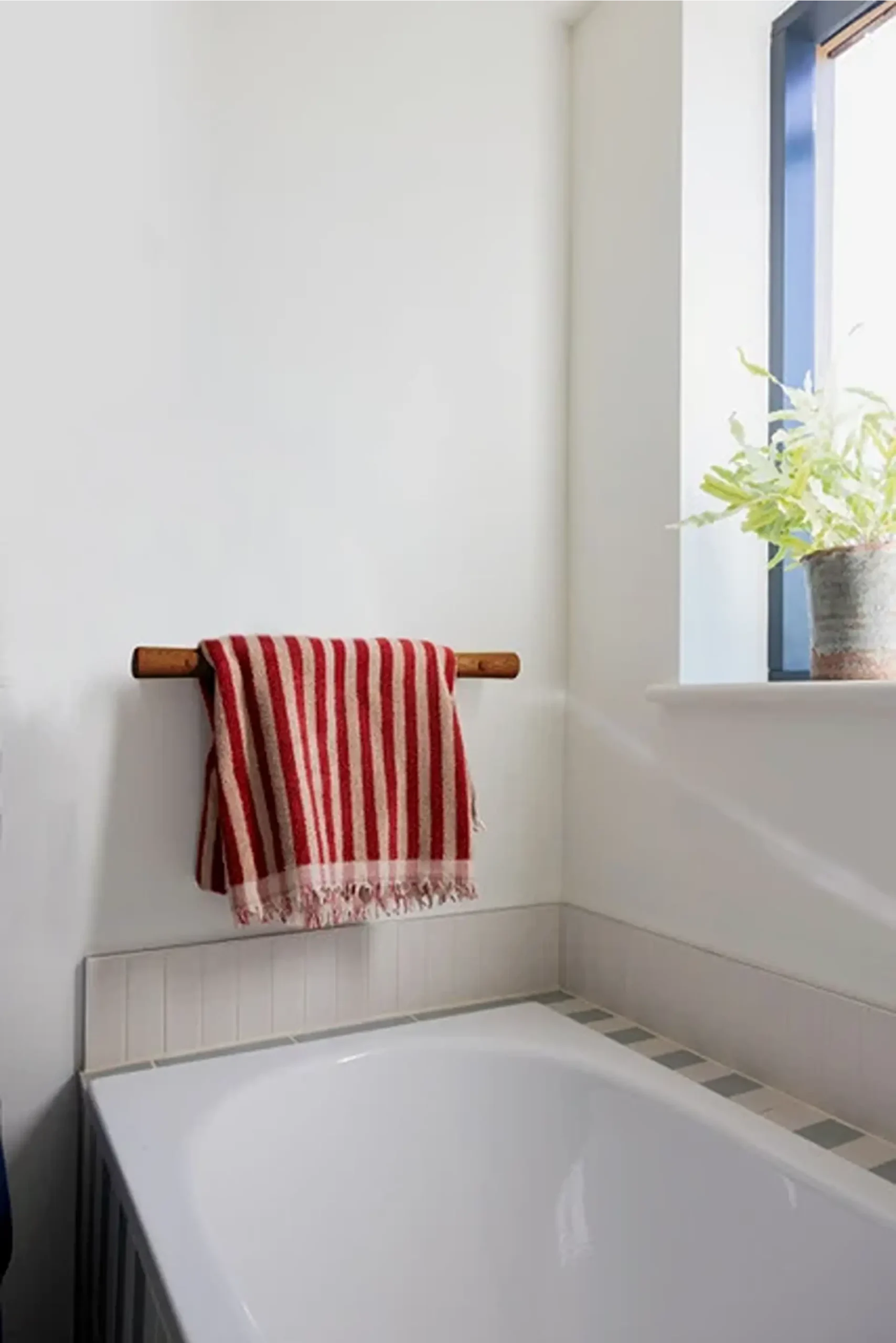Striped towel hanging over an oak grab rail above a bathtub.