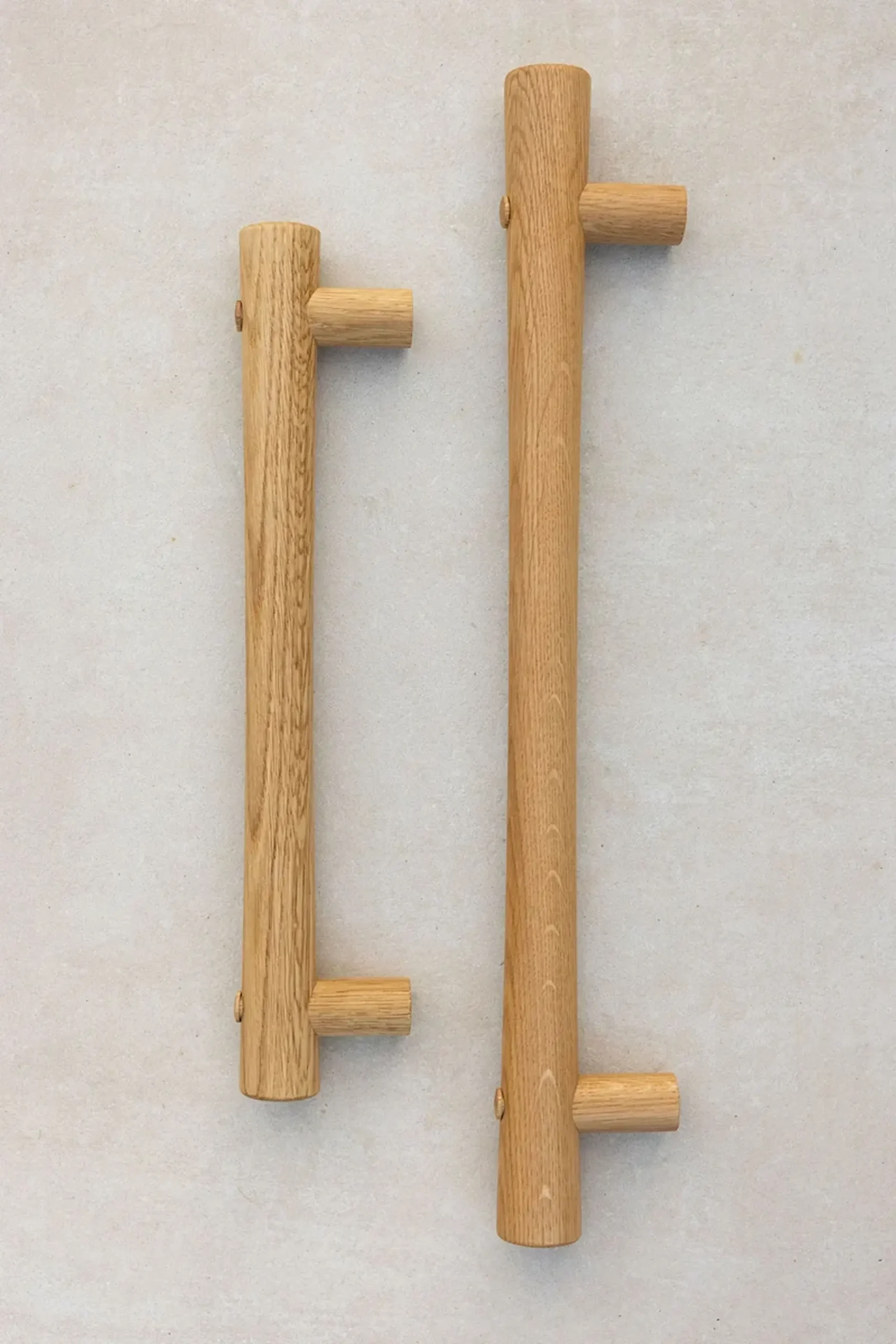 Two oak grab rails with T-ends standing upright on a light surface.